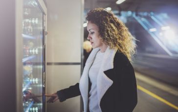 Attractive woman on transit platform using a modern beverage vending machine.Her hand is placed on the dial pad and she is looking on the small display screen.